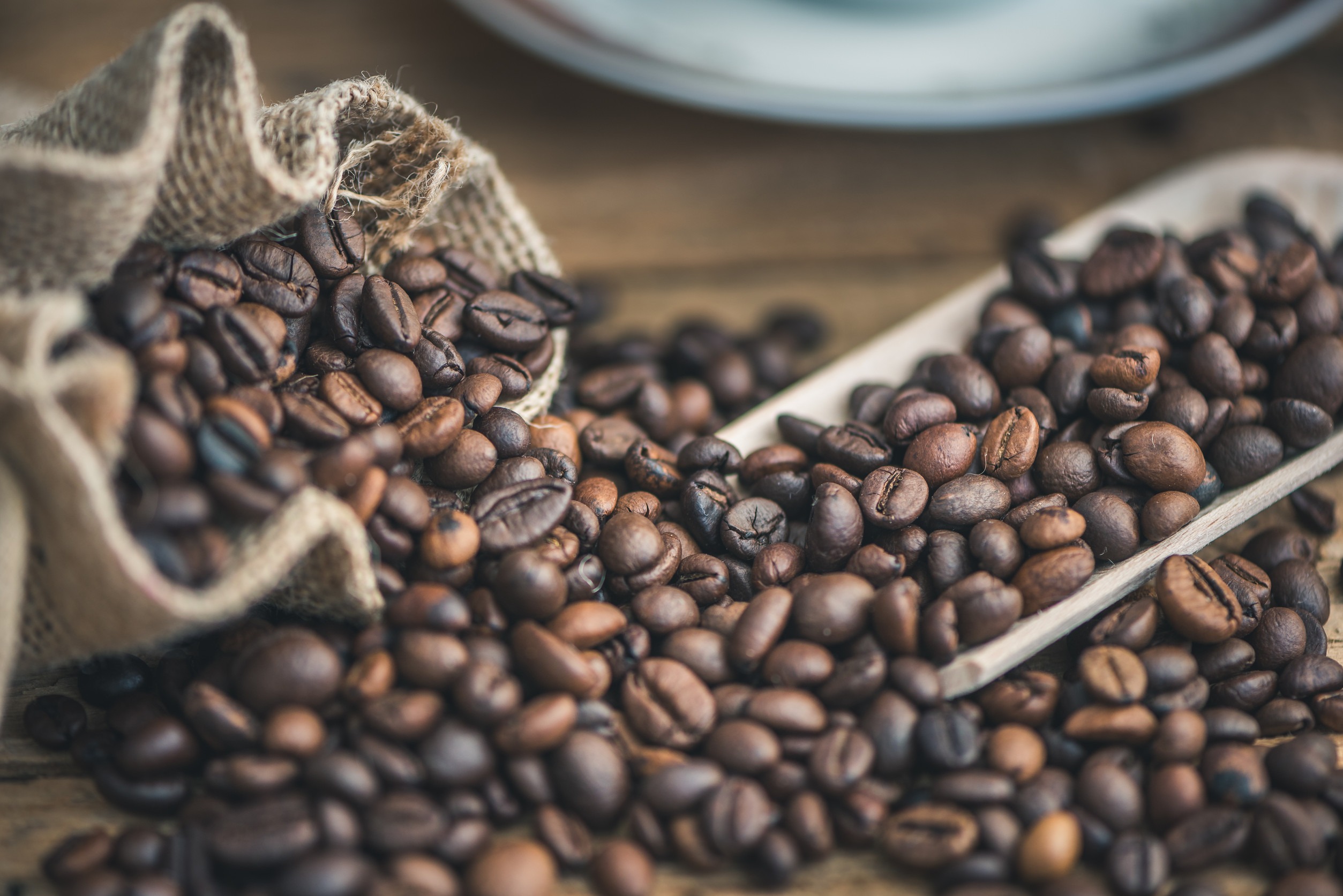 Roasted-Coffee-Beans-Spilled-out-of-Burlap-Sack-on-Wooden-Background