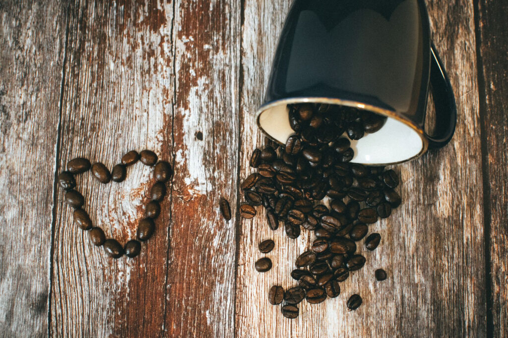 Coffee beans spilling from a mug beside a heart made of coffee beans.